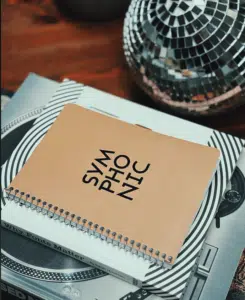 A spiral-bound notebook with "SYMPHONIC" on the cover rests on a stack of books near a reflective mosaic sphere.